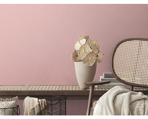 Helle Inneneinrichtung mit Blumen in Vase und Rattansessel vor rosafarbener Wand