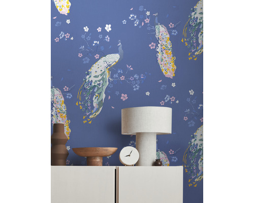 Dekoratives Interieur mit Tapete mit Pfauenmuster, Tischlampe und Wohnaccessoires auf einem Sideboard