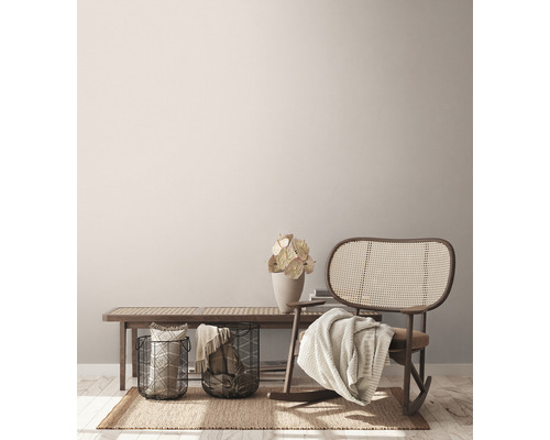Wohnzimmerszene mit Bank, Rattanschaukelstuhl, Körben und Dekoration auf einem Teppich.