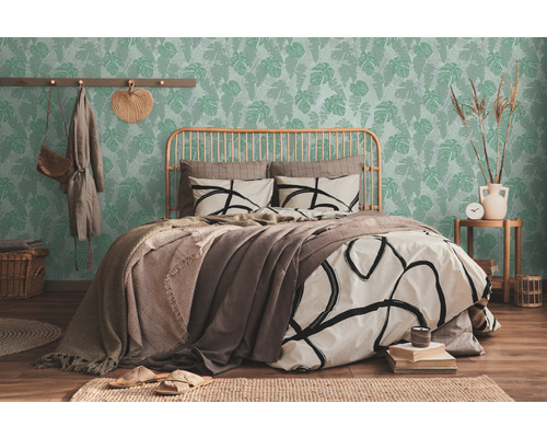 Chambre lumineuse avec lit devant un papier peint vert à motifs de feuilles