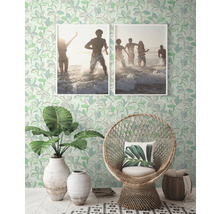 Dekoratives Zimmer mit gemusterter Tapete, Rattan-Sessel, Pflanzen und gerahmten Fotos.