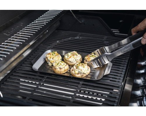 Champignons farcis sur une plaque de gril avec des pinces de barbecue sur un gril.