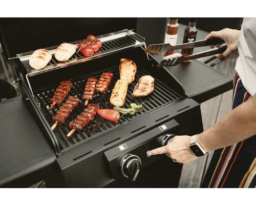 Barbecue à gaz avec grillades et personne utilisant une pince à grill