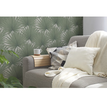 Wohnzimmer mit grauer Couch, Kissen, Decke und gemusterter Tapete mit Palmenmotiven