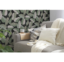 Dekoratives Wohnzimmer mit einer Couch, Kissen und einer Wandtapete mit Blättermotiv.