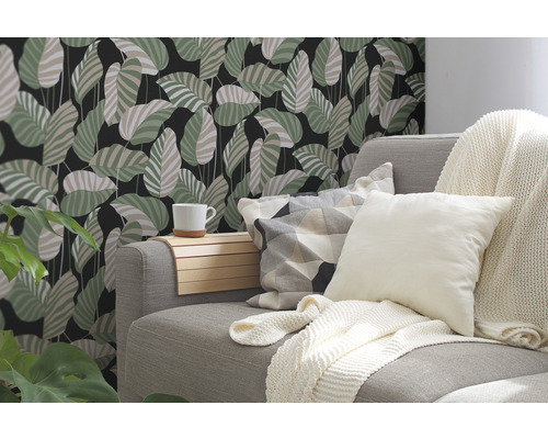 Dekoratives Wohnzimmer mit einer Couch, Kissen und einer Wandtapete mit Blättermotiv.