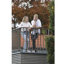 Zwei Personen auf einem Balkon mit Metallgeländer vor Bäumen.