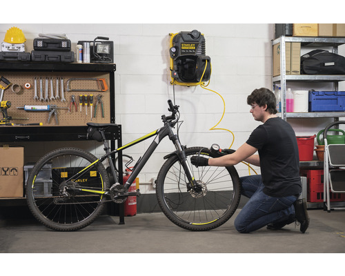 Mann pumpt Fahrradreifen mit einem Kompressor in einer Werkstatt auf.