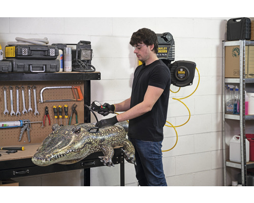 Mann pumpt aufblasbares Krokodil auf einer Werkbank mit Werkzeugen auf