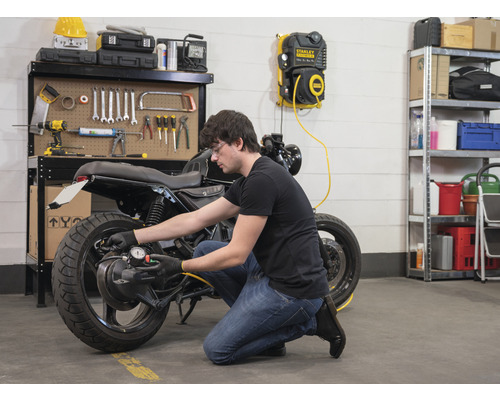 Mann prüft Reifendruck eines Motorrads mit Luftkompressor in Werkstatt