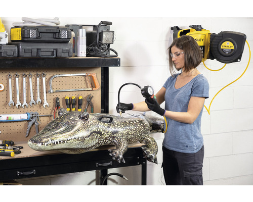 Frau pumpt aufblasbaren Alligator mit Luftdruckmesser an Werkbank auf.