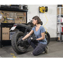 Une femme vérifie la pression des pneus d''une moto dans un garage avec un compresseur mural.