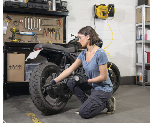 Frau überprüft den Reifendruck eines Motorrads in einer Garage mit einem an der Wand montierten Kompressor