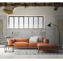 Wohnzimmer mit orangefarbenem Ledersofa, Ottomanen, Teppich und Stehlampe vor einem Fenster