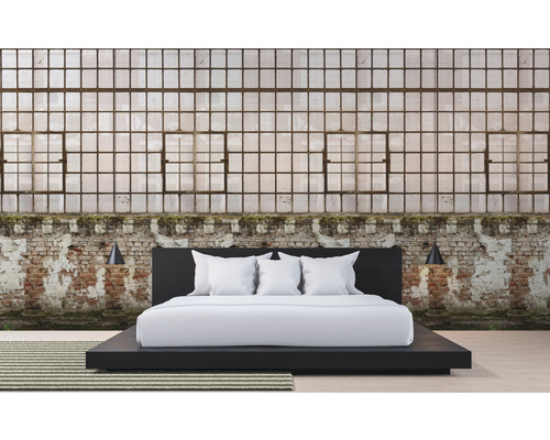 Schlafzimmer mit einem Bett vor einer Ziegelwand und großen Fenstern