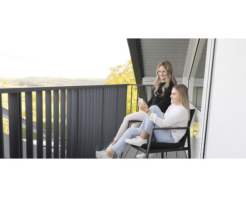 Deux jeunes femmes sont assises sur un balcon avec une balustrade et profitent de la vue.