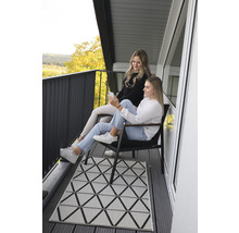 Szene auf einem Balkon mit zwei Frauen, Stühlen und einem Teppich mit geometrischem Muster.