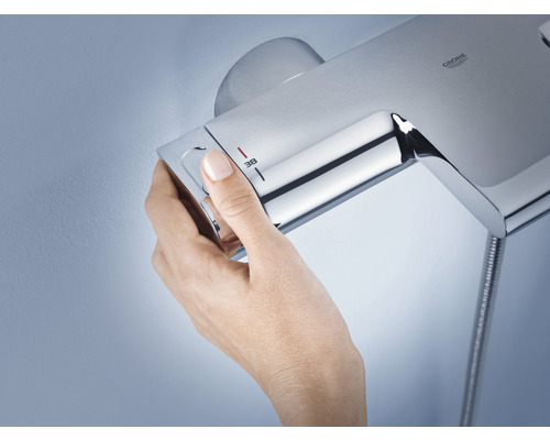 Une main règle la température sur une robinetterie de douche Grohe