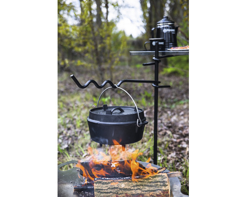Gusseisen-Topf über offenem Feuer an einem Dreibein mit Campingtisch und Zubehör im Freien