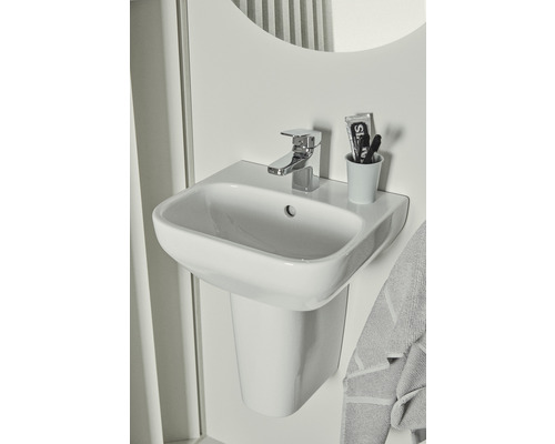Lavabo blanc avec robinet, brosse à dents et dentifrice dans une salle de bain.