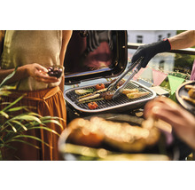 Personen grillen Gemüse und Fleisch auf einem Grill.