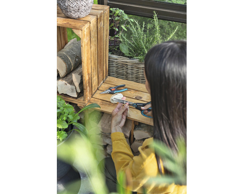 Une femme coupe de la ficelle avec un sécateur à côté de caisses en bois et de plantes.
