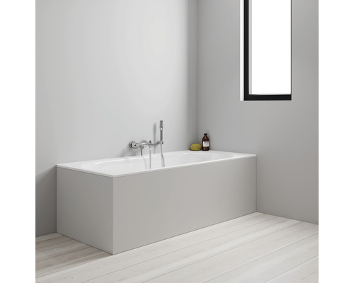 Baignoire avec habillage, robinetterie et produits de soin dans la salle de bain.