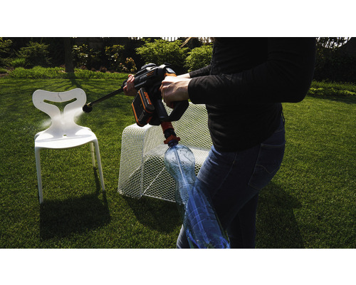 Une personne utilise un nettoyeur haute pression sans fil pour nettoyer une chaise en plastique dans le jardin. Une bouteille d''eau est connectée au nettoyeur haute pression.
