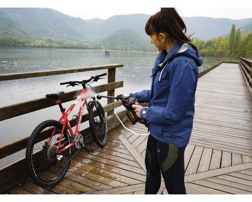 Une femme nettoie un vélo avec un nettoyeur haute pression sur une jetée en bois au bord d''un lac.