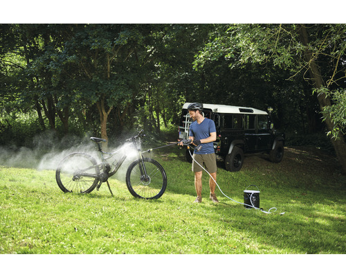 Un homme nettoie un vélo avec un nettoyeur haute pression mobile à l''extérieur.