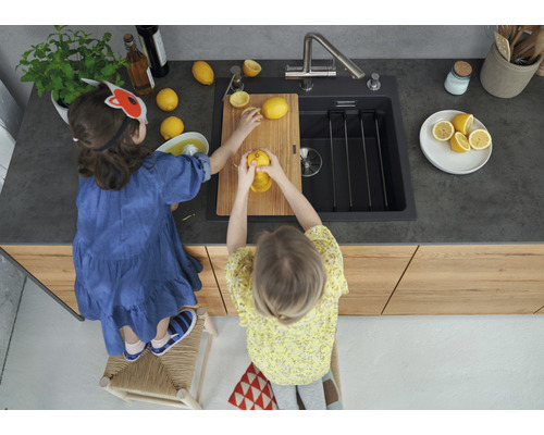 Deux enfants préparent du jus de citron sur une planche à découper dans une cuisine avec évier.