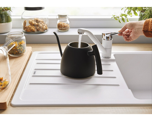 Eine Hand bedient einen Wasserhahn über einer Spüle, die eine schwarze Teekanne befüllt.