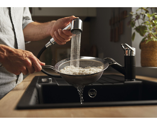 Mann spült Reis in einem Sieb unter einem Küchenarmatur