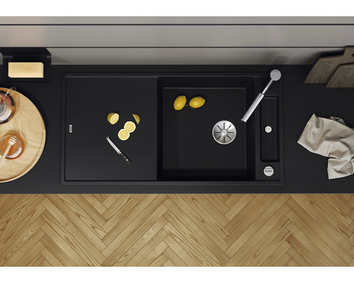 Évier noir avec égouttoir, robinet, citrons et couteau sur un plan de travail.