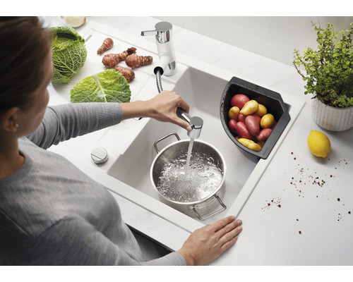 Frau befüllt Topf mit Wasser an einer Spüle mit Gemüse und Kartoffeln