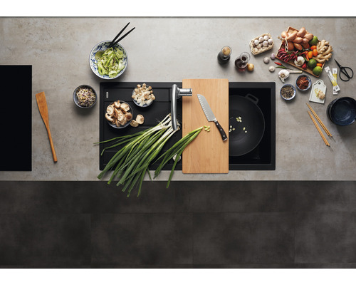 Évier de cuisine avec robinetterie, planche à découper, couteau, wok et divers ingrédients pour la préparation de plats asiatiques.