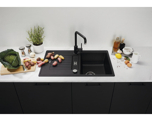 Schwarze Küchenspüle mit Abtropffläche und Armatur auf einer Küchentheke mit Lebensmitteln