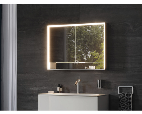 Salle de bains moderne avec armoire de toilette éclairée, lavabo et robinet.