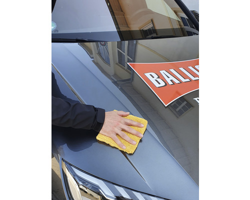 Une personne nettoie le capot d''une voiture avec un chiffon jaune.