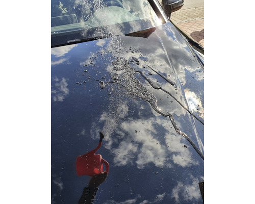 De l''eau est versée sur une voiture avec un arrosoir, créant un effet perlant
