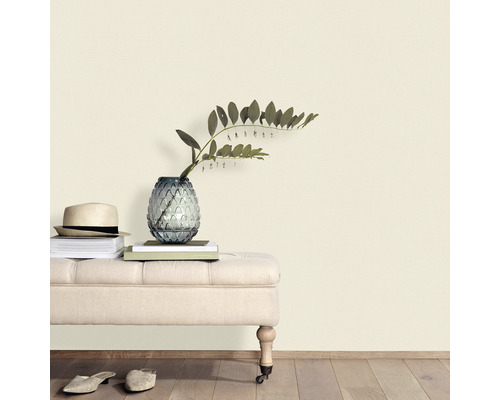 Dekorative Szene mit Sitzbank, Vase, Pflanzen, Büchern und Hut vor einer Wand.