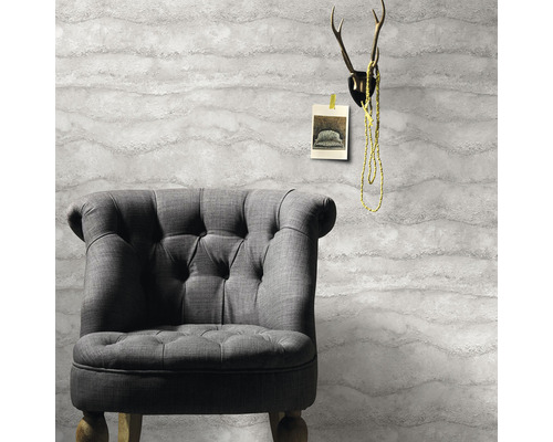 Grauer Sessel vor einer Tapete mit Wellenmuster, darüber ein Geweih