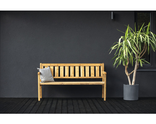 Banc en bois avec coussin et plante en pot devant un mur sombre