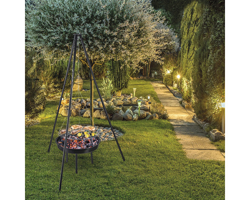 Grill mit Dreibein im Garten mit Bäumen, Steinen und Rasen