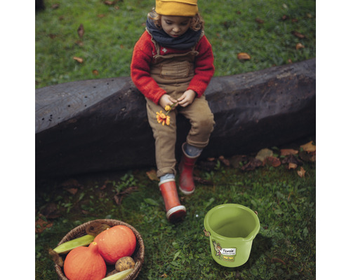 Szene mit Kind, Kürbissen im Korb und einem grünen Eimer auf einer Wiese