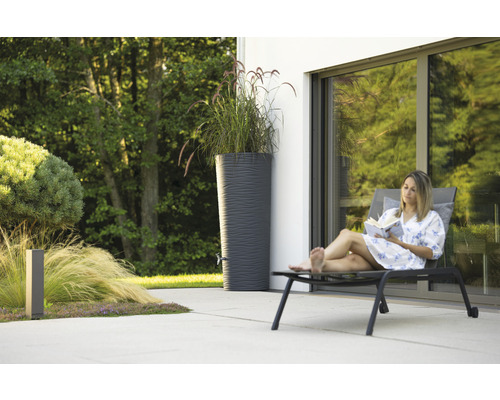Femme lisant un livre à côté d''un récupérateur d''eau de pluie dans le jardin.