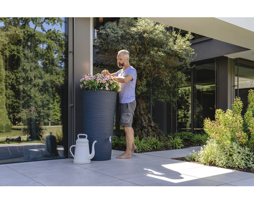 Un homme plante des fleurs dans un récupérateur d''eau de pluie dans un jardin