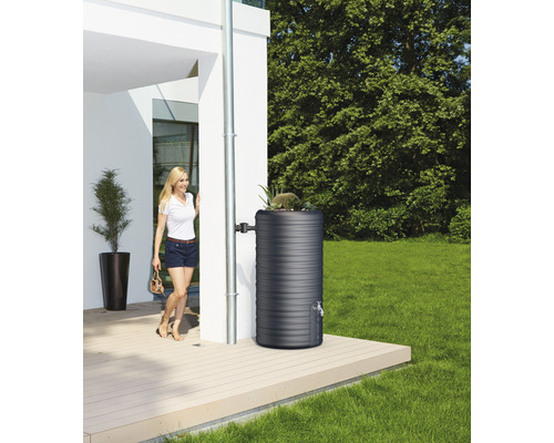 Récupérateur d''eau de pluie dans le jardin à côté d''une maison avec une femme