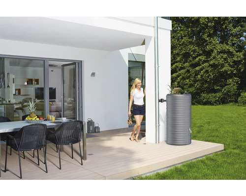 Réservoir d''eau de pluie en plastique à côté d''une descente pluviale sur une maison moderne avec terrasse.