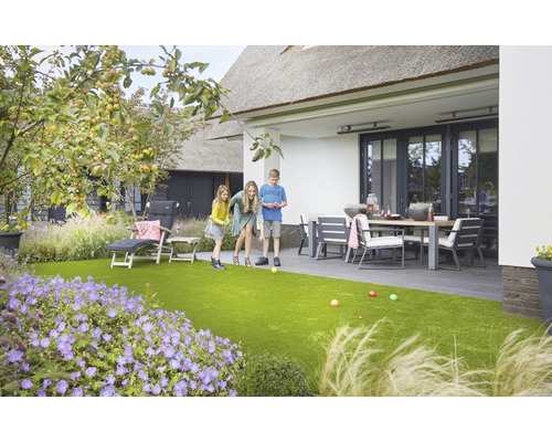 Famille jouant à la pétanque dans le jardin avec gazon synthétique, mobilier de jardin et plantes